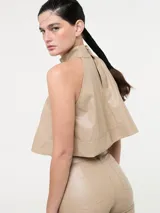 Top corto color beige, estilo halter con cuello alto y espalda descubierta. Confeccionado en eco cuero.
