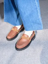 Mocasines Mutma Gales de cuero color tostado, con plataforma gruesa dentada, detalles de tachas metálicas, argollas y tira lateral con hebilla.