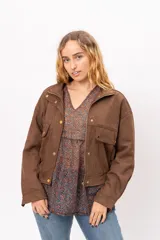 Chaqueta bomber de efecto gamuza en color marrón, con cierre frontal de cremallera y botones metálicos a presión. Presenta bolsillos frontales con solapa y terminación elastizada en la cintura.