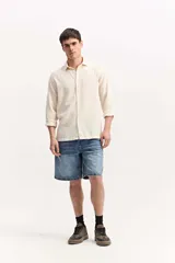 Camisa de manga larga color beige, de tejido texturado con cierre frontal de botones y cuello camisero clásico.