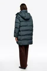 Campera tipo plumífero de largo medio con silueta en línea A, confeccionada en tejido técnico brillante. Presenta cierre frontal con cremallera, cuello subido con capucha desmontable, mangas largas con puños interiores de pelo sintético y bolsillos laterales con cremallera.