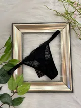Tanga de encaje negro con tiras finas ajustables y refuerzo de algodón.
