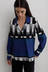 Camisa de manga larga con cuello solapa y cierre frontal de botones. Presenta un diseño estampado con bloques geométricos en tonos azul, blanco y negro.