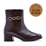 Bota corta de cuero color marrón oscuro, con taco cuadrado bajo y punta cuadrada. Presenta una correa delgada con hebilla dorada alrededor del tobillo.