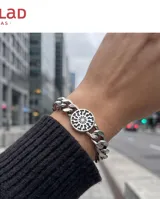 Pulsera de eslabones tipo grumet fabricada en acero, con un dije central circular que presenta un diseño grabado de rueda solar.