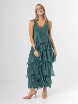 Vestido largo negro de seda italiana con diseño sin mangas de bretel ancho y escote en V profundo con detalles de paillettes plateados. Presenta múltiples capas con volados y bordes deshilachados que aportan movimiento y una caída fluida.