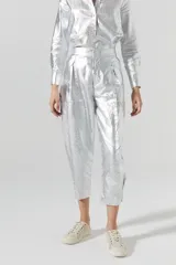 Pantalón slouchy plateado de lino orgánico con efecto metalizado y gastado. Tiene tiro medio, pinzas, cierre frontal, bolsillos laterales y traseros, y ajuste en los tobillos.