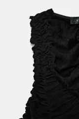 Top negro sin mangas con escote pico profundo y detalle de frunces o drapeado en todo el frente. El ruedo inferior tiene un borde festoneado.