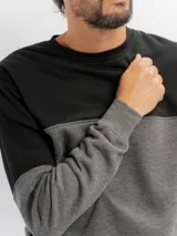 Buzo de felpa de diseño colorblock con cuello redondo, mangas largas y puños de rib, combinando negro en la parte superior y azul en la inferior y mangas.