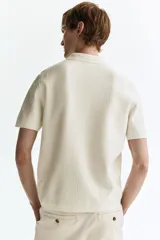 Remera polo de manga corta de H&M en punto texturizado color blanco, con cuello clásico, tapeta con botones y ribetes acanalados en puños y bajo.