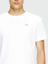 Remera blanca de manga corta con cuello redondo y un pequeño logo bordado en color rosado en el pecho.