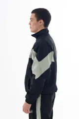 Campera negra de nylon con recortes en forma de V en color gris en las mangas. Tiene cuello mao, cierre frontal, puños y cintura elásticos, bolsillos laterales y logo estampado en el pecho y en la manga izquierda.