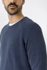 Sweater de punto en color azul marino, con cuello redondo y mangas raglán. Presenta un tejido acanalado fino y puños elásticos.