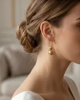 Caravanas colgantes de acero con baño de oro, compuestas por un gancho alargado y una esfera metálica lisa en el extremo inferior.