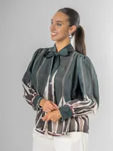 Camisa de manga larga con cuello alto y lazo para atar, confeccionada en tela liviana con estampado geométrico en tonos verde oscuro, blanco, beige y marrón.