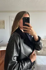 Campera bomber corta de napalan negro con interior forrado en piel sintética color azul noche. Presenta cierre frontal, cuello con solapas y detalles de pasamanería en cruz a lo largo de las mangas.