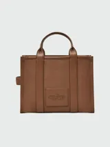 Bolso tipo tote de cuero negro, modelo The Leather Medium Tote Bag de Marc Jacobs. Presenta doble asa superior, correa ajustable para el hombro y el texto grabado "THE TOTE BAG MARC JACOBS" en el frente.