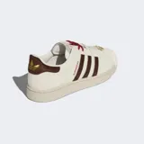 Championes Adidas Superstar II con exterior de cuero y material sintético en color blanco crema. Presentan las icónicas tres tiras laterales y refuerzo en el talón en color marrón oscuro texturizado, puntera de goma con relieve y suela de caucho al tono.