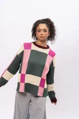 Buzo de tejido de punto con diseño geométrico de cuadros en tonos verde oscuro, rosa y crema. Presenta cuello redondo, puños y ruedo en color bordó, con mangas largas y corte holgado.