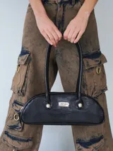 Cartera estilo baguette de cuero negro con textura tipo reptil. Presenta un diseño estructurado de silueta alargada, con manijas largas y detalles de nudos esféricos metálicos en la unión de las mismas. Incluye una placa metálica con el logo de la marca en el centro.