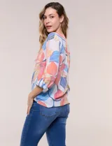Blusa estampada Zac & Rachel con diseño floral en tonos rosados, azules y amarillos sobre base blanca. Presenta escote en V con botones frontales, mangas tres cuartos con presilla para arremangar y detalle de nudo en el ruedo.