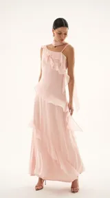 Vestido largo de fiesta color rosa pastel, confeccionado en tela fluida con diseño de un solo hombro y detalle de volados en cascada que recorren el frente y el lateral. Incluye un pañuelo integrado al cuello del mismo tejido.