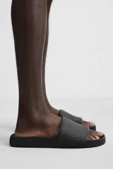 Chancla tipo pala monocolor negra, con suela de goma y tira ancha en el empeine con relieve acanalado.