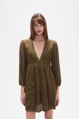 Vestido corto de color verde militar, con escote en V profundo, mangas largas con puños elásticos y detalles de encaje y bordados en el frente. Presenta una falda con vuelo y textura de pequeños puntos en relieve.