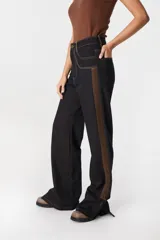 Jean de tiro alto y pierna recta, confeccionado en denim color azul oscuro. Presenta una franja lateral en tono marrón, costuras en contraste y tajos en el ruedo. Cuenta con diseño de cinco bolsillos y cierre frontal.