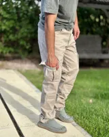 Pantalón cargo de corte holgado, color arena, confeccionado en gabardina elastizada. Presenta bolsillos laterales con solapa en los muslos, costuras reforzadas en las rodillas y cierre frontal con botón y cremallera.