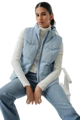 Chaleco acolchado tipo puffer con diseño western, confeccionado en denim de lavado claro. Presenta cuello alto, cierre frontal con cremallera y costuras horizontales.