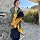 Ruana de material símil cachemira, de diseño bicolor en tonos gris y lila con bandas anchas en los bordes.