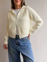 Cardigan tejido de textura suave con cierre frontal de doble vía, cuello alto y mangas largas. Presenta terminaciones en rib en puños y cintura, con un diseño versátil y moderno.