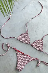 Conjunto de bikini con corpiño triangular de atar con apliques de argollitas y bombacha vedetina de atar con apliques de argollitas. El tejido presenta un estampado tie-dye o marmolado en tonos lila/azul y naranja/beige.