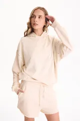 Buzo canguro con capucha color beige, confeccionado sin friza, con detalles de tachas aplicadas en la capucha y las mangas.
