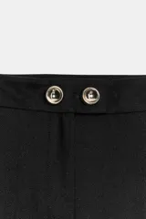 Pantalón negro de tiro medio con pierna ancha y cierre frontal de cremallera con dos botones dorados decorativos.