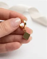 Caravanas tipo argolla con dije colgante en forma de rombo, acabado en tono dorado.
