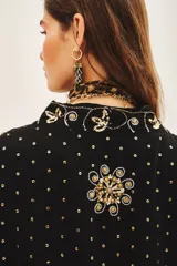 Kimono de corte holgado en color negro, con mangas tres cuartos y diseño bordado con motivos florales y detalles en hilo dorado. Presenta un cierre frontal anudado y forro interior.