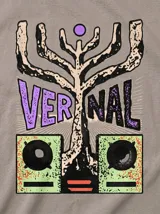 Remera de algodón color gris topo con corte relajado. Presenta un diseño gráfico estampado en la espalda que combina una figura abstracta con parlantes en tonos violeta y verde ácido.