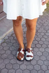 Suecos con capellada de cuero con estampado de vaca, plantilla anatómica y hebilla lateral ajustable.