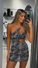 Vestido corto ajustado, negro con estampado geométrico de líneas plateadas brillantes. Diseño asimétrico de un solo hombro con un corte en la cintura.
