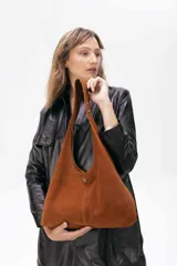 Cartera tipo hobo de cuero ovino color suela, con diseño amplio y flexible. Presenta un aplique metálico pequeño en el frente y costura central vertical.