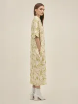 Vestido camisero de corte oversize, con cuello clásico, cierre frontal de botones y mangas cortas. Presenta un estampado floral en tonos verde y beige, bolsillos laterales y un diseño holgado.