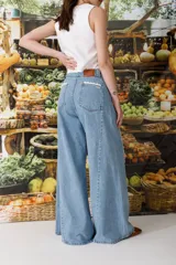 Jean de corte wide leg con diseño de tiro alto y piernas amplias. Presenta detalles de puntilla de crochet en los bolsillos delanteros y a lo largo de las costuras laterales, aportando un estilo romántico y distintivo.
