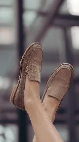 Mocasines de gamuza color tostado, con diseño clásico de pespuntes marcados en la parte delantera y suela plana.