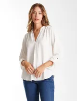 Blusa de color blanco con escote en V y cuello mao. Presenta mangas largas con presilla y botón para regular el largo, y un corte holgado con ruedo redondeado.