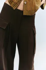 Pantalón cargo de tiro medio en color marrón oscuro, con corte recto y amplio. Presenta bolsillos laterales tipo cargo con solapa y detalle de pliegues frontales. Cierre frontal con cremallera y botón.