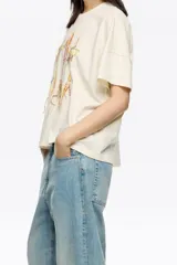 Camiseta de manga corta, corte oversize, color marrón oscuro. Presenta un estampado frontal con el texto "BIMBA Y LOLA" realizado con hilos de colores vibrantes que cuelgan, simulando un bordado texturizado.