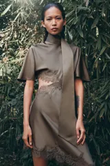 Vestido midi satinado de cuello subido y manga corta tipo capa. Presenta aberturas laterales con aplicación de encaje a tono y bajo asimétrico con detalle de encaje. Incluye un pañuelo integrado en el mismo tejido y cierre posterior con botones forrados.