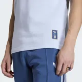 Remera Adidas de la colección Originals inspirada en la selección de Italia. Es de color celeste claro con cuello redondo y mangas cortas, presenta las tres tiras características de la marca en azul sobre los hombros y mangas. Incluye el logo del Trifolio de Adidas en el lado derecho del pecho y el escudo de la selección italiana en el lado izquierdo.